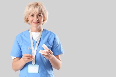 Açık arkaplanda çene modeli ve aracı olan kadın dişçi