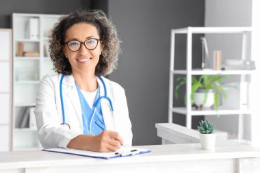 Klinikteki resepsiyonda panoya yazı yazan olgun bir kadın doktor.