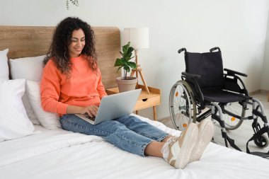 Tekerlekli sandalyesi ve dizüstü bilgisayarı olan genç Afro-Amerikalı kadın evde yatıyordu.