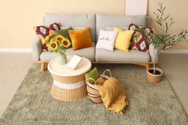 Şık oturma odasının içinde rahat bir kanepe, sehpada ayçiçeği vazosu ve zeytin ağacı.