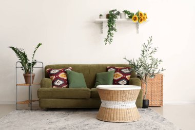 İçinde yeşil kanepe, sehpa, çiçek ve zeytin ağacı olan güzel bir oturma odası.