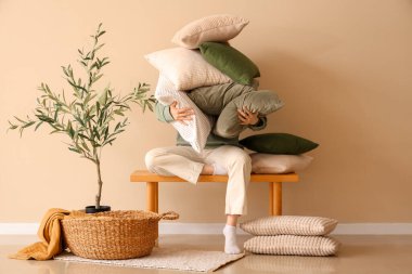 Genç bir kadın şık bir odada yumuşak yastık yığınıyla bankta oturuyor.