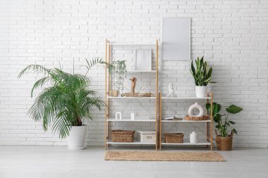 Odadaki beyaz tuğla duvarın yanında heykelciği ve bitkisi olan raf ünitesi.