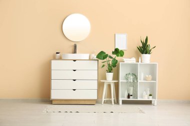 Seramik lavabo, raf ünitesi ve banyoda bej duvarın yanındaki çekmeceler.