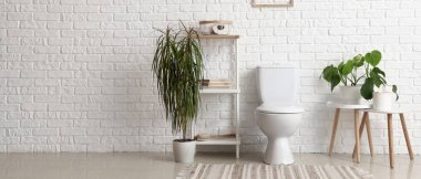 Seramik klozet, raf ünitesi ve beyaz tuğla duvarın yanındaki evlerin olduğu ışık tuvaleti. Tasarım için pankart