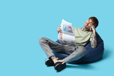 Mavi arka planda gazetesi olan puf minderli yakışıklı bir genç.