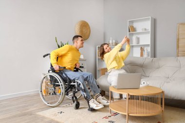 Tekerlekli sandalyedeki genç adam ve kız arkadaşı evde selfie çekiyorlar.