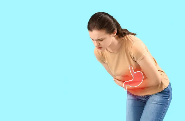 stock image Young woman suffering from pain in stomach on light blue background