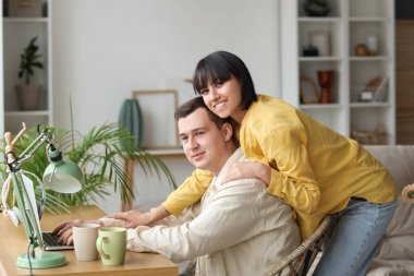 Aşık genç çift evdeki masada dizüstü bilgisayar kullanıyor.