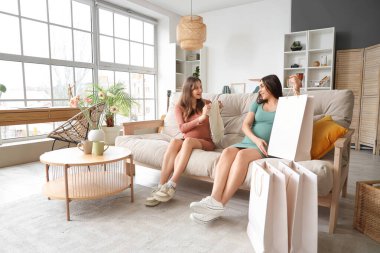 Hamile bayan arkadaşlar evdeki kanepede oturuyor.