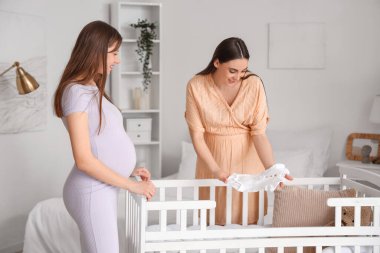 Hamile bayan arkadaşlar yatak odasındaki bebek beşiğinin yanında.