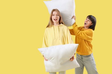 Sarı arka planda yastıklarla savaşan genç kadınlar