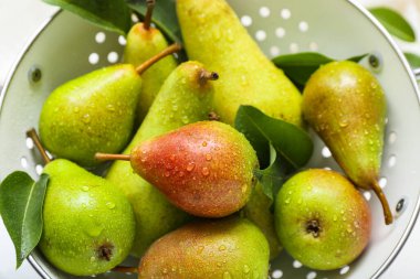 Beyaz mermer masa üzerinde olgun armutlarla Colander, yakın plan.