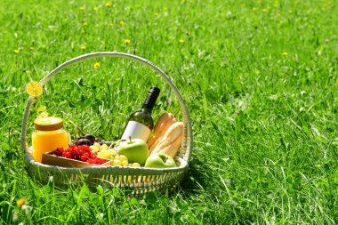 Parktaki çimlerde romantik piknik için lezzetli yiyecek ve içeceklerle dolu bir sepet.