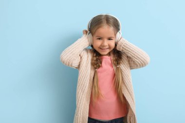 Kulaklıklı mutlu küçük kız mavi arka planda müzik dinliyor.