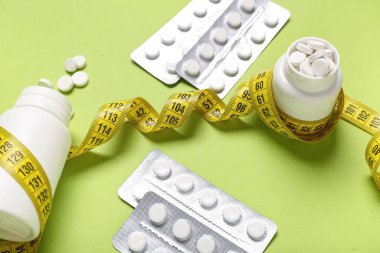 Kilo verme hapları, su toplamaları ve yeşil arka planda şerit bulunan şişeler.