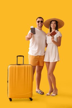 Güzel, genç, mutlu, bavul, pasaport ve sarı arka planda biletleri olan iki turist.