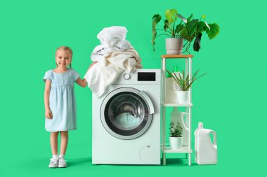 Kirli çamaşırları olan küçük bir kız yeşil arka planda çamaşır yıkıyor.