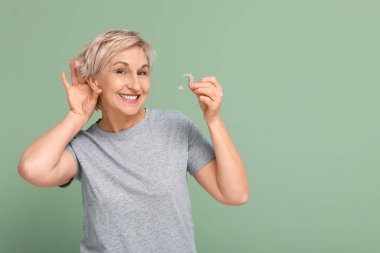 Yeşil arka planda işitme cihazı olan olgun bir kadın.
