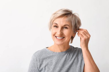 Olgun kadın beyaz arka planda kulağına işitme cihazı takıyor.