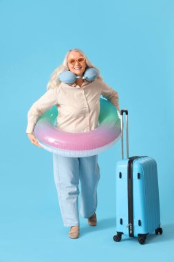 Yüzme yüzüğü ve bavulu olan olgun bir kadın mavi arka planda yaz tatiline hazır.