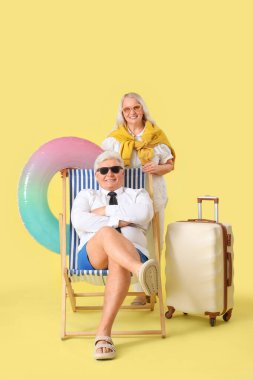 Yüzme yüzüğü ve bavulu olan olgun iş adamları sarı arka planda yaz tatiline hazır.