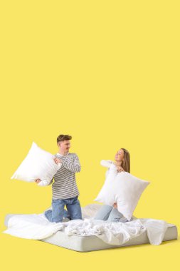 Sarı arka planda döşek üzerinde kavga eden genç çift