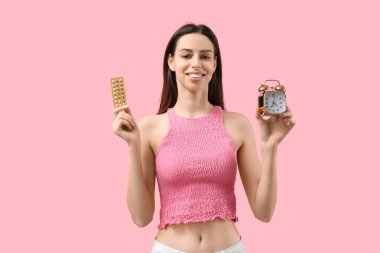 Doğum kontrol hapları ve pembe arka planda çalar saati olan güzel bir kadın.