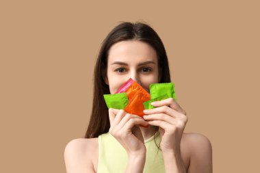 Kahverengi arka planda prezervatifleri olan güzel bir genç kadın.