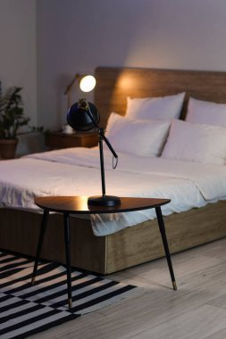 Glowing lamp on table in bedroom at night
