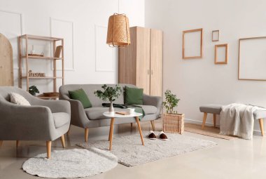 Gri kanepenin yanındaki halıda terlikler. Oturma odasının içinde şık bir iç mekan.