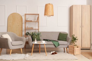 Gri kanepenin yanındaki halıda terlikler. Oturma odasının içinde şık bir iç mekan.