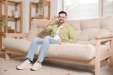 Evdeki kanepede oturan gözlüklü yakışıklı genç adam.