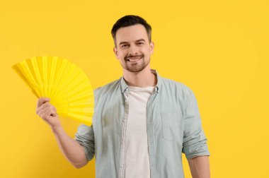 Sarı arka planda yelpazesi olan genç bir adam