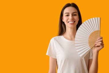 Turuncu arka planda el yelpazesi olan genç bir kadın.