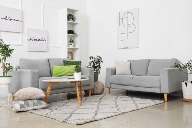 Modern oturma odasındaki gri kanepe, çiçekler, resimler ve kahve masası.