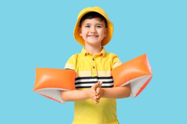 Panama şapkalı şirin bir çocuk ve mavi arka planda şişme kolluklar.