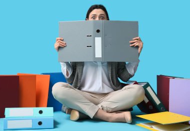 Dosyaları mavi arka planda oturan güzel genç iş kadını.