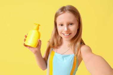 Burnunda güneş kremi ve sarı arka planda bir şişe krem olan güzel bir kız.