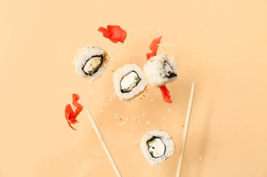 Bej arka planda lezzetli uçan suşi ruloları, zencefil ve çubuklar.