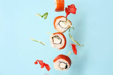 Lezzetli uçan suşi ruloları, mavi arka planda zencefil ve salatalık.