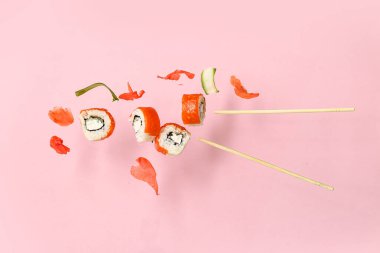 Nefis uçan suşi ruloları, zencefil, salatalık ve pembe arka planda çubuklar.