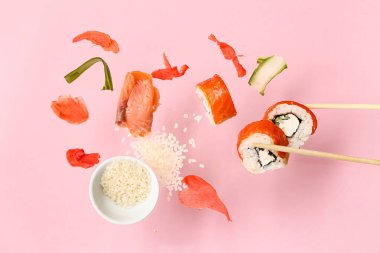 Nefis uçan suşi ruloları, malzemeler ve pembe arka planda çubuklar.