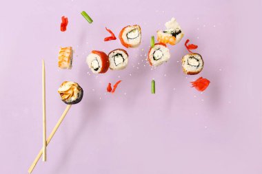 Lezzetli uçan suşi ruloları ve leylak arka planda çubuklar.