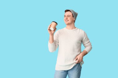 Şapkalı genç adam ve mavi arka planda bir fincan kahve.