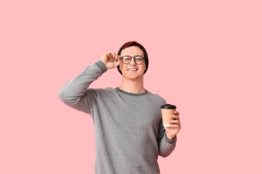 Şapkalı genç adam, pembe arka planda gözlüklü ve bir fincan kahveli.