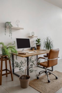 Ofis duvarının yanında bilgisayar monitörü ve ev bitkileri olan modern işyeri