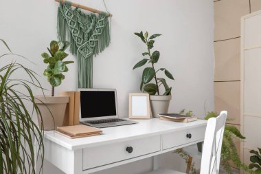 Ofis duvarının yanında dizüstü bilgisayarı ve bitkileri olan modern bir işyeri.