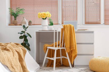 Modern dizüstü bilgisayarı ve beyaz masasında sarı narsisli çiçekleri olan rahat çalışma alanı.