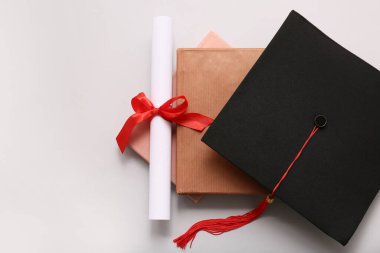 Kırmızı kurdeleli diploma, kitaplar ve beyaz arka planda mezuniyet şapkası.